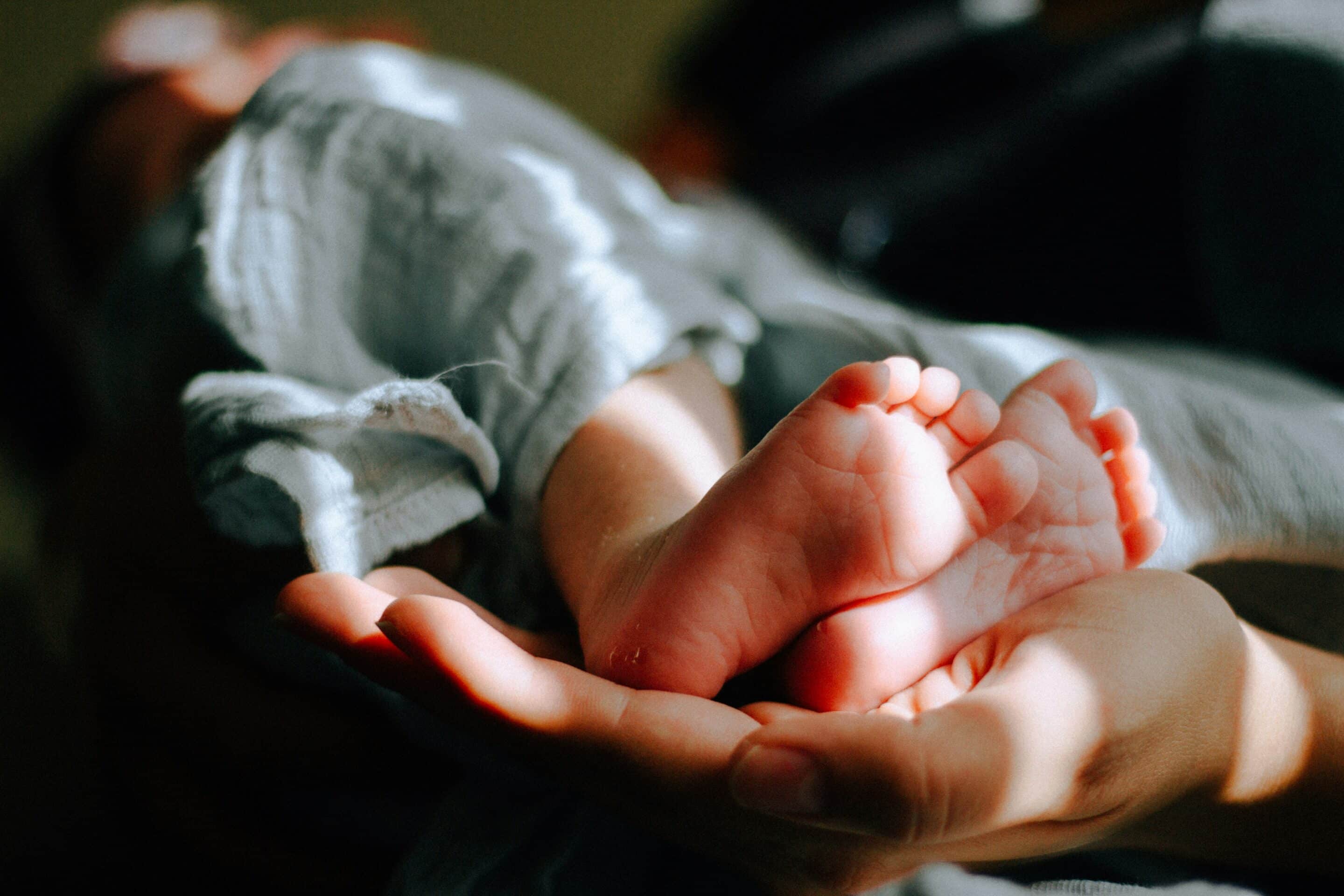 A baby's feet are held, toward the camera, in the palm of a hand.