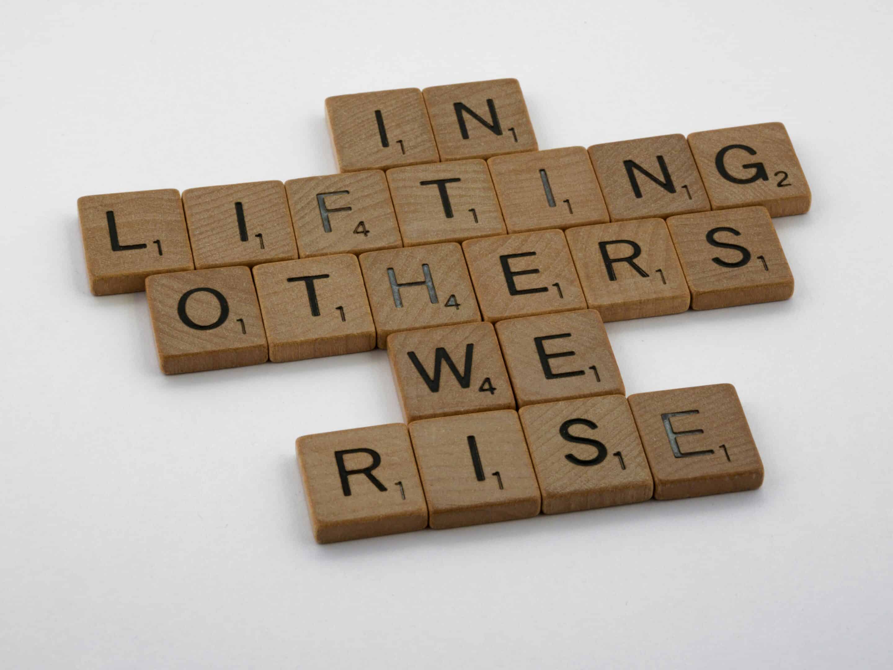 Scrabble tiles say in lifting each tother we rise