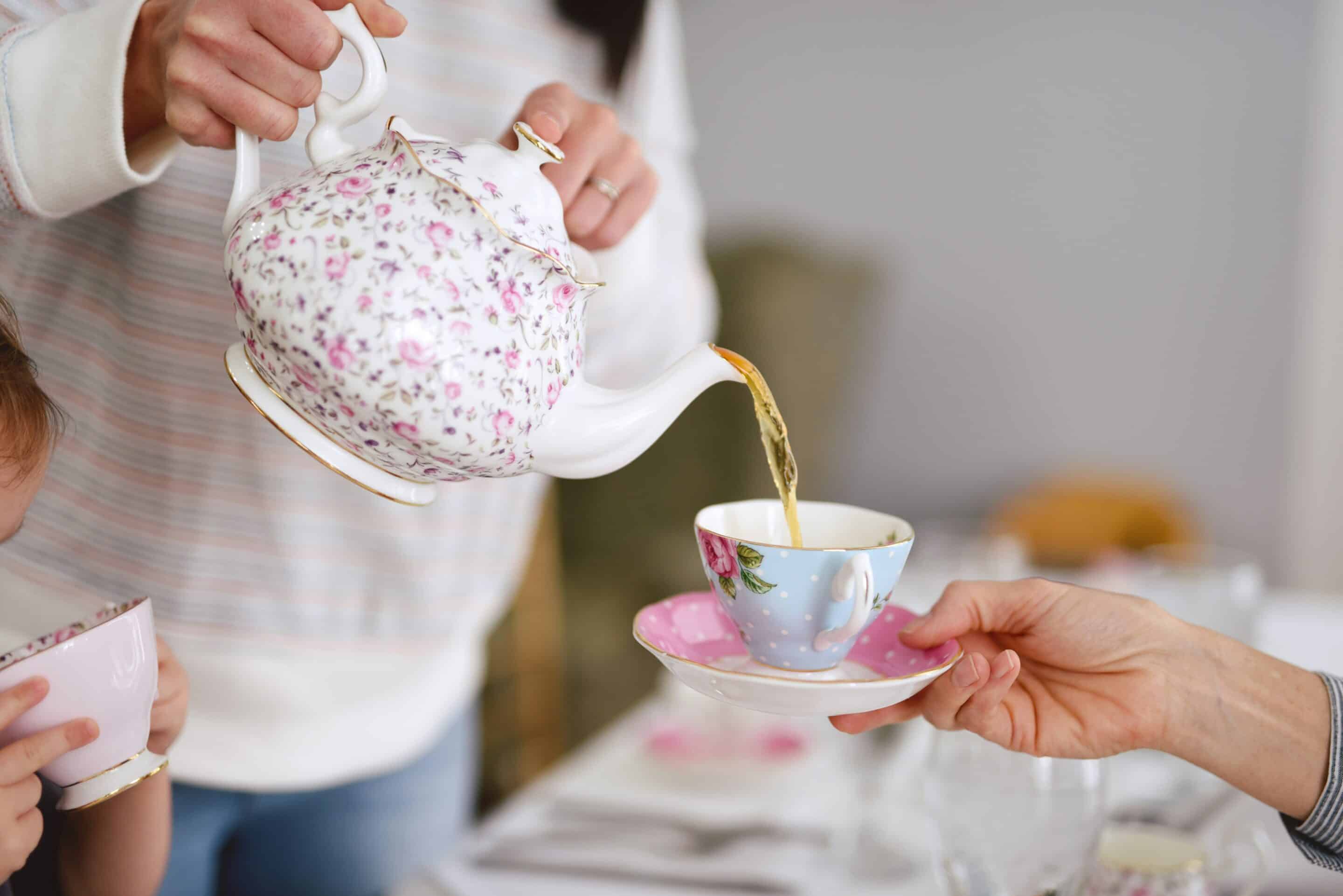 A lady pours tea into a cup from a china tea pot