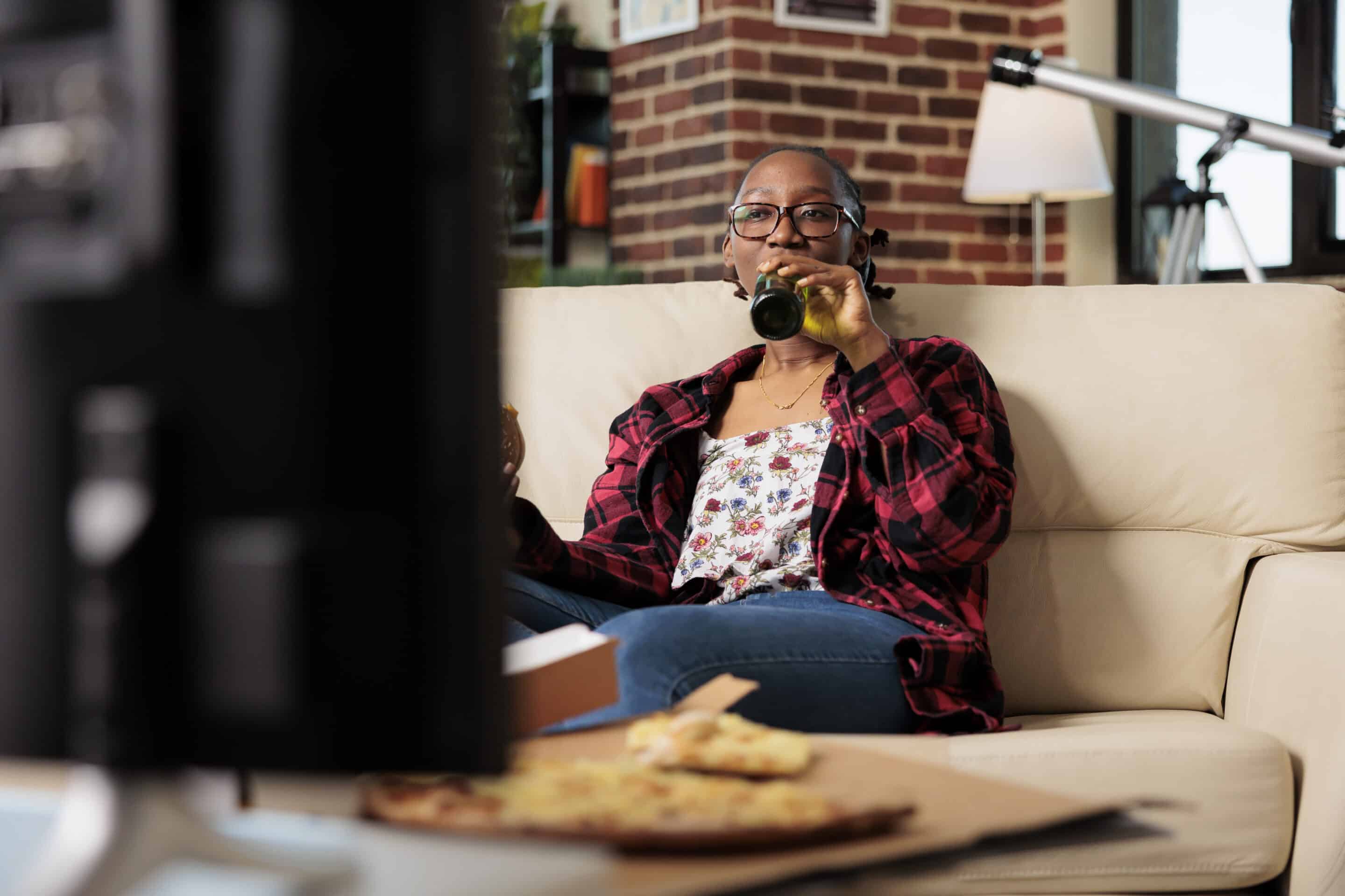 Cheerful adult drinking alcoholic beer from bottle on couch